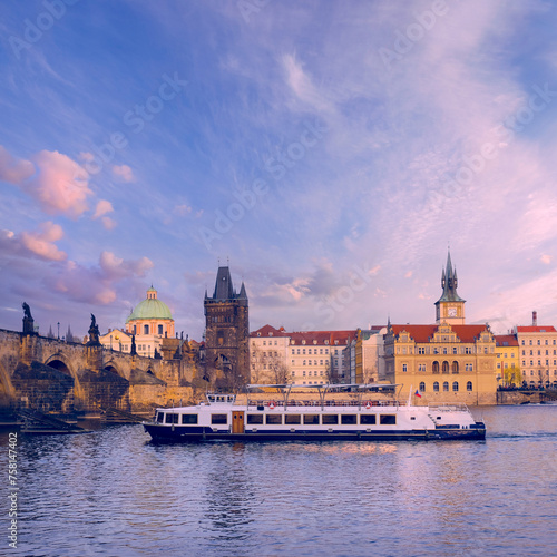 A boat glides on the water in front of a grand castle, surrounded by spring flowers along the Prague River.