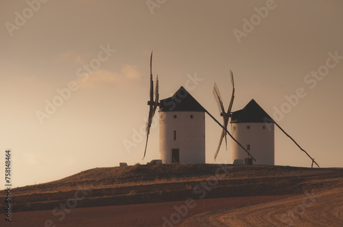 Top of the hill crowned by two traditional whitewashed windmills facing the sun while the day ends. Campo de Criptana windmills. photo