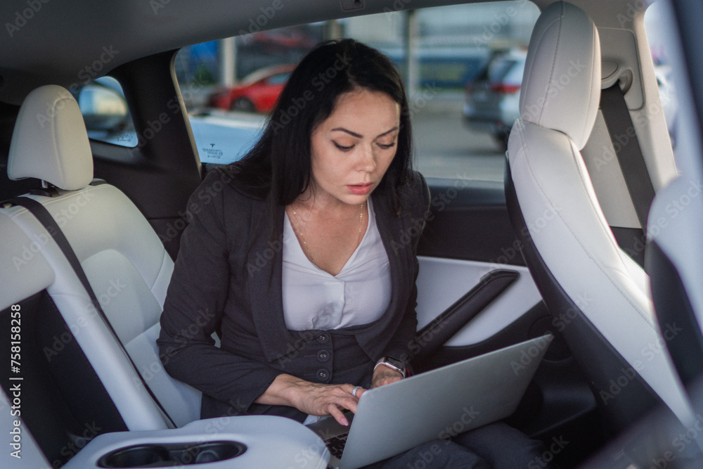 Attentive businesswoman working with laptop, looking at screen, typing while sitting on the back seat of car. Business, road trip, technology, travel concept