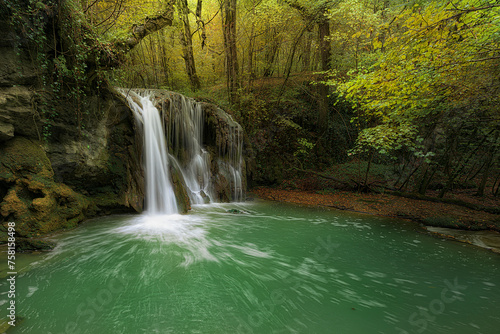 Altube waterfall in Alava at the beginning of autumn with the foliage beginning to change color and the river water an intense emerald color