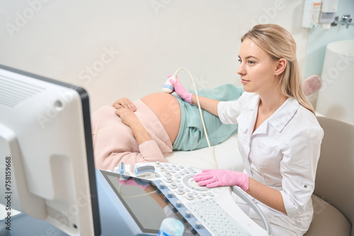 Young qualified sonographer making ultrasound to pregnant woman photo