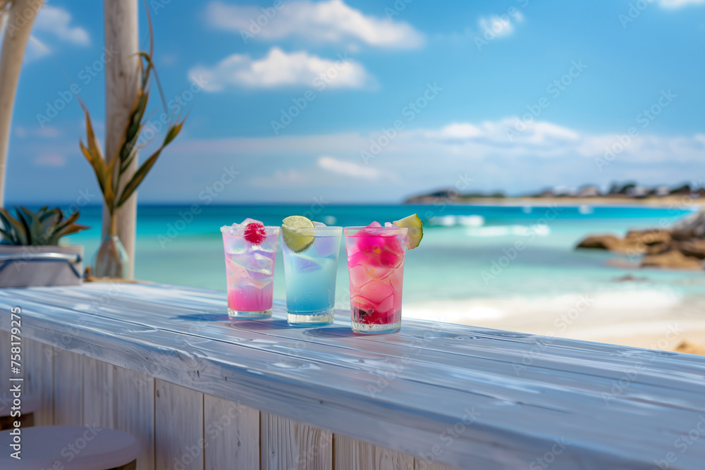 Variety of coctails and alcoholic drinks and multi colored on the reflective wooden surface of bar counter. Blurred cristal clear water white sand beach on background 