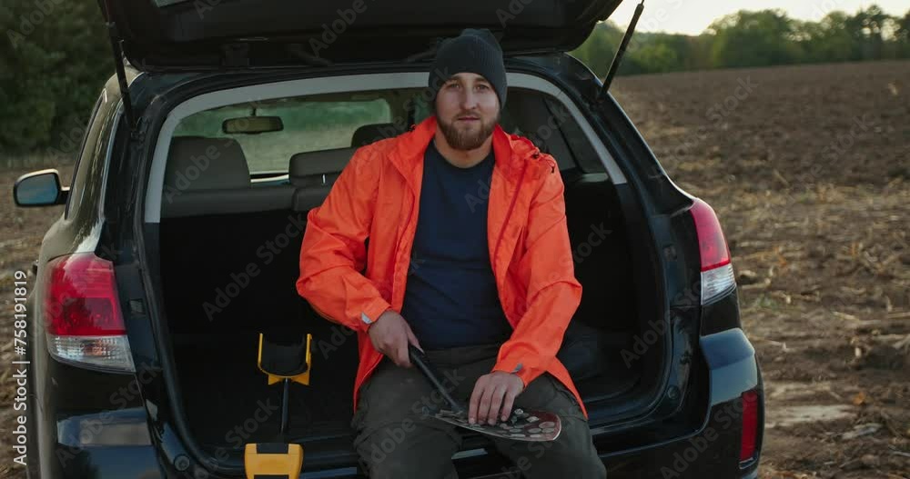A male archaeologist sits in the trunk of a car holding ancient coins found with a metal detector. A male archaeologist sits in the trunk of a car holding ancient coins found with a metal detector.