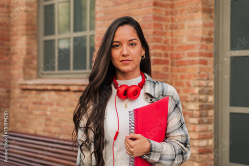 Close up individual portrait of a pretty hispanic female student with serious expression looking at camera at high school. Head shot of latin teenage girl standing outdoors at the university campus photo