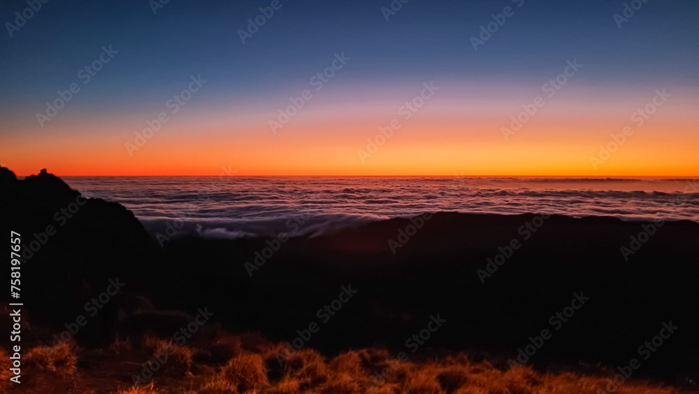 Panoramic view of sunrise seen from top Pico do Areeiro, Madeira island, Portugal, Europe. First sunlight touching surface of illuminated clouds covering the Atlantic Ocean. Dramatic red orange sky