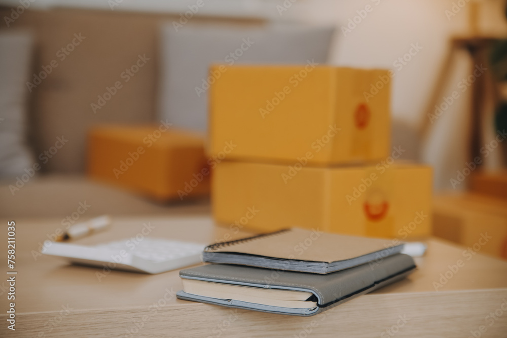 Asian SME business women use laptop computer checking customer order online shipping boxes at home. Starting Small business entrepreneur SME freelance. Online business, Work at home concept. Asian SME business women use laptop computer checking customer order online shipping boxes at home. Starting Small business entrepreneur SME freelance. Online business, Work at home concept.