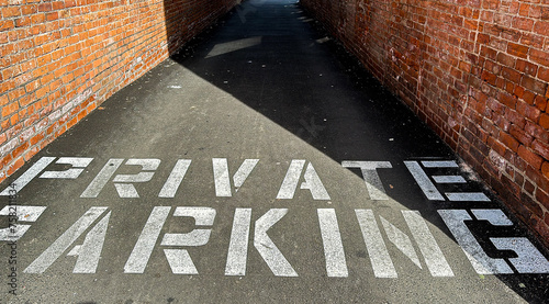 Private parking text painted on asphalt walkway between brick walls with available copy space photo