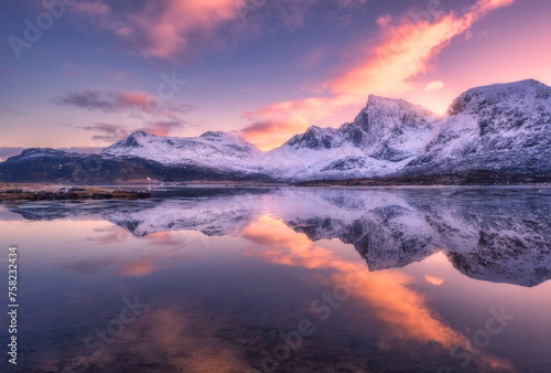 Beautiful snowy mountains and colorful sky with clouds at sunset in winter in Lofoten islands  Norway. Landscape with rocks in snow  sea coast  reflection in water at dusk  purple sky with pink clouds