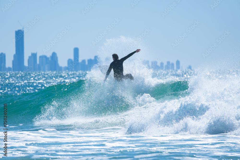 Young man surfing a wave in the blue sea with view of skyscrapers behind in Gold Coast, Australia