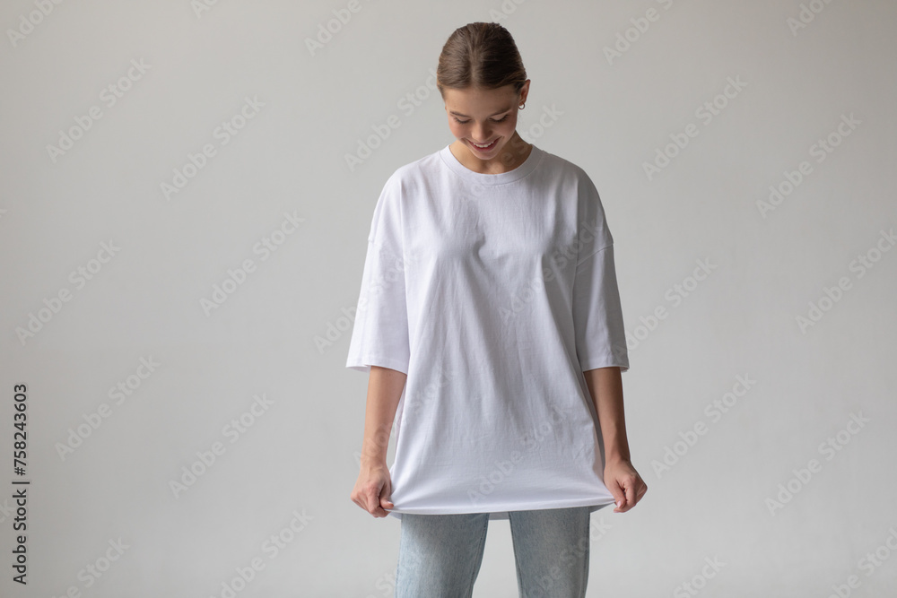 Beautiful blonde girl in a white oversized T-shirt and blue jeans posing on a gray background Beautiful blonde girl in a white oversized T-shirt and blue jeans posing on a gray background