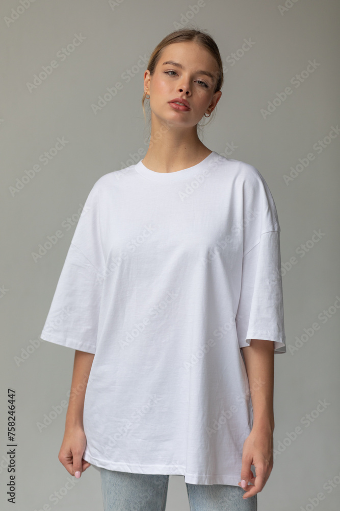 Beautiful blonde girl in a white oversized T-shirt and blue jeans posing on a gray background Beautiful blonde girl in a white oversized T-shirt and blue jeans posing on a gray background