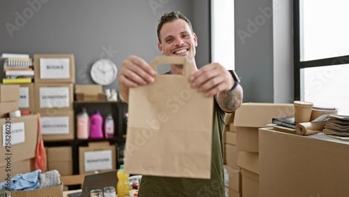 Smiling young man with a beard holding a paper bag in a warehouse surrounded by boxes and office supplies. photo