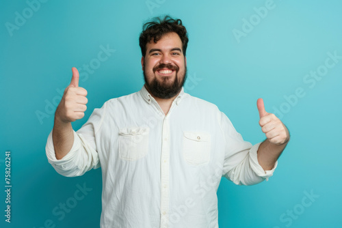 Young happy plump plus size man showing thumbs up isolated on plain blue background