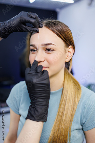 Marking a woman's face before a permanent eyebrow tattoo procedure. Women's master of permanent make-up