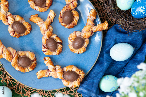 gedrehter und gefüllter Blätterteig mit Marmelade und einem Ei aus Schokolade zu einem kleinen Hase als Süßspeise zu Ostern im Frühling