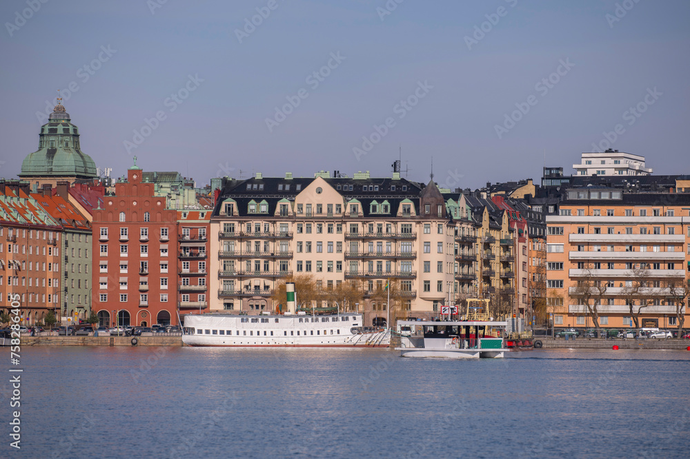 The waterfront at the bay Riddarfjärden in the island Kungsholmen, apartment houses, a steam passengers ferry and an electrical powered small cross bay ferry a sunny winter day in Stockholm