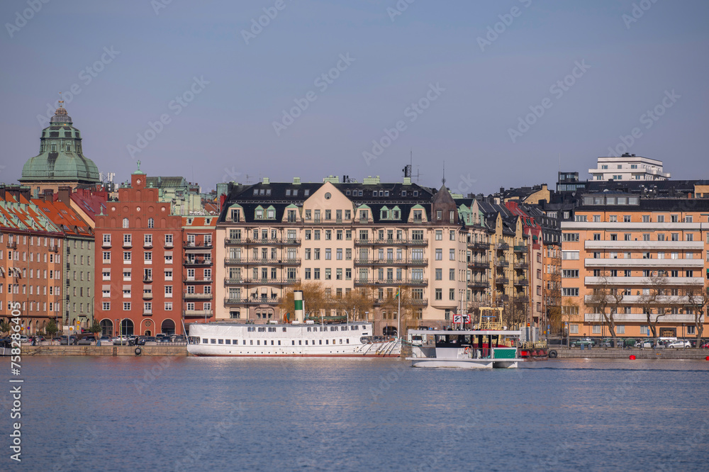 The waterfront at the bay Riddarfjärden in the island Kungsholmen, apartment houses, a steam passengers ferry and an electrical powered small cross bay ferry a sunny winter day in Stockholm The waterfront at the bay Riddarfjärden in the island Kungsholmen, apartment houses, a steam passengers ferry and an electrical powered small cross bay ferry a sunny winter day in Stockholm