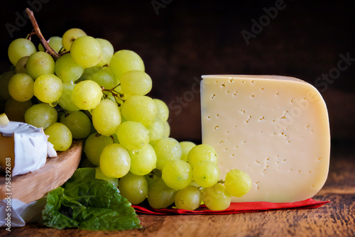 Still life, appetizing arrangement of green grapes and a piece of cheese against a dark background.