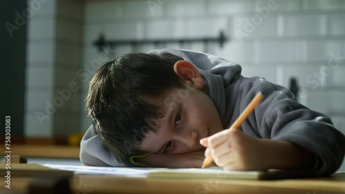Tired little schoolboy kid lying on table desk writing homework, boring class lesson drawing in notebook at home.