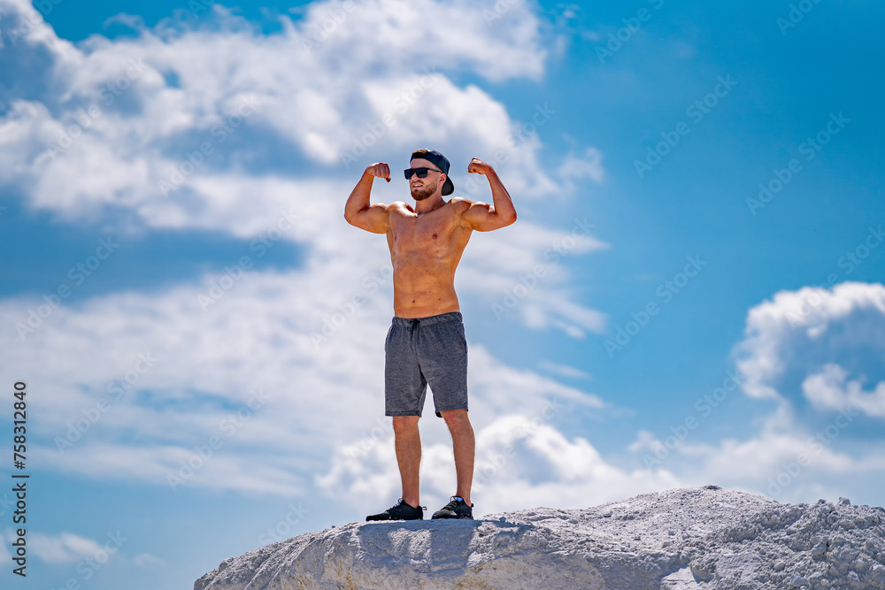 Young muscular man standing on rock and flexing his arms Young muscular man standing on rock and flexing his arms