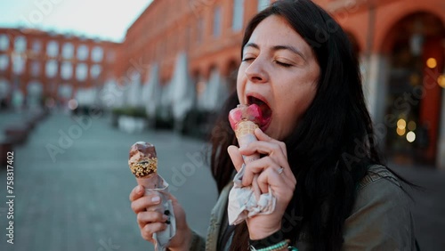 Woman enjoying two ice creams standing in European city eating cone gelato, 30s female person indulgence photo