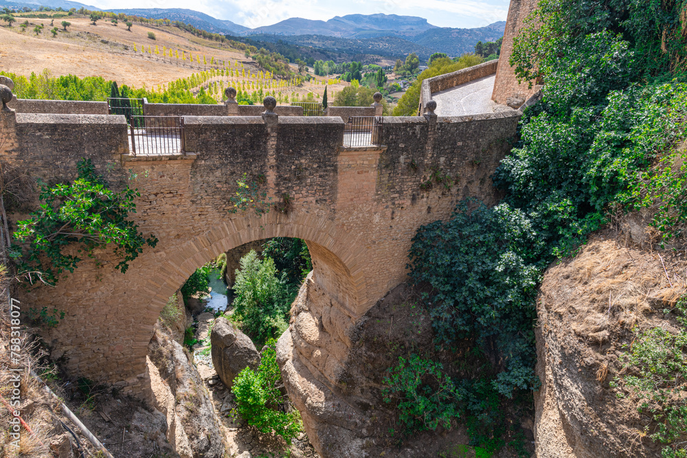 View of old stone arched Puente Viejo bridge crossing rocky river in mountainous valley in Ronda, Andalusia, Spain