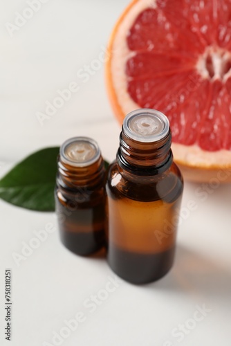 Grapefruit essential oil in bottles, leaf and fruit on white table © New Africa