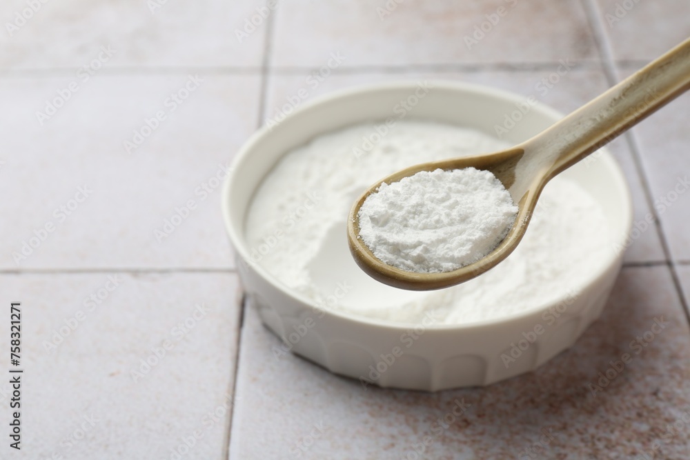 Spoon of baking powder over bowl at light tiled table, closeup. Space for text Spoon of baking powder over bowl at light tiled table, closeup. Space for text