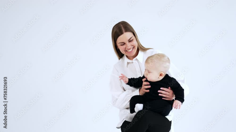 Happy smiling woman in white shirt holding a blond baby wearing black suit. Child with cute plump cheeks sits peacefully on mom's laps. Happy smiling woman in white shirt holding a blond baby wearing black suit. Child with cute plump cheeks sits peacefully on mom's laps.