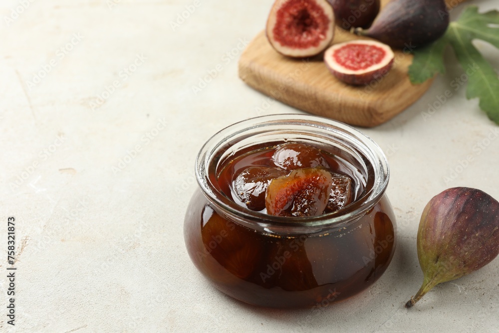 Jar of tasty sweet jam and fresh figs on white table, space for text Jar of tasty sweet jam and fresh figs on white table, space for text