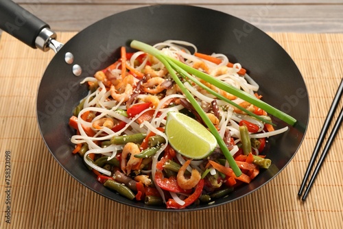 Shrimp stir fry with noodles and vegetables in wok on table