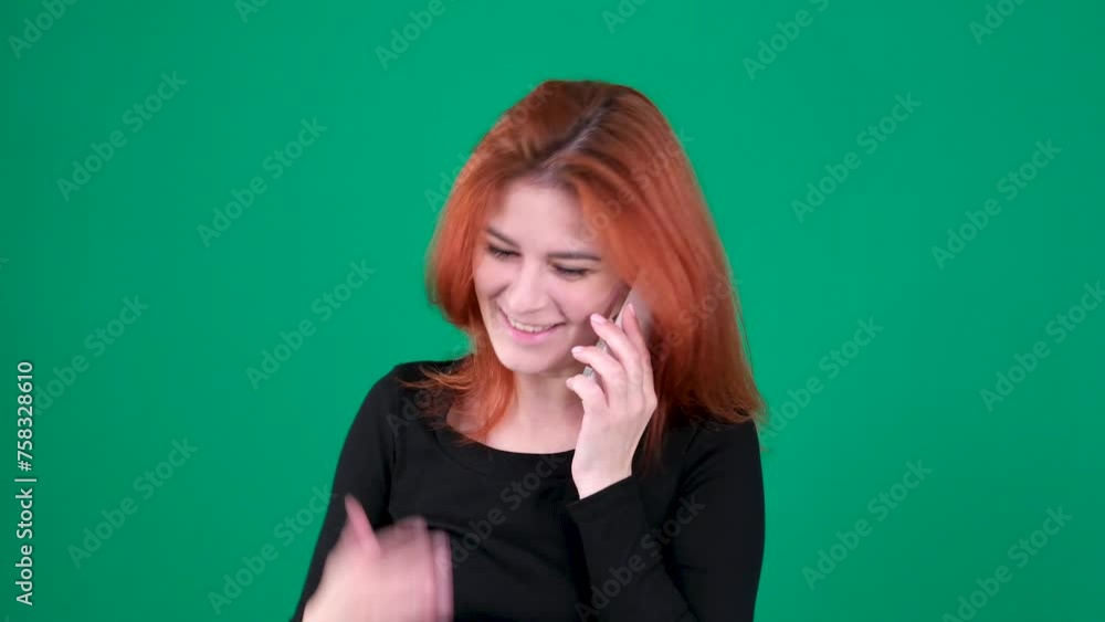 Red-haired girl talking on White phone, smiling, satisfied, happy. Green background. Hand gestures Red-haired girl talking on White phone, smiling, satisfied, happy. Green background. Hand gestures