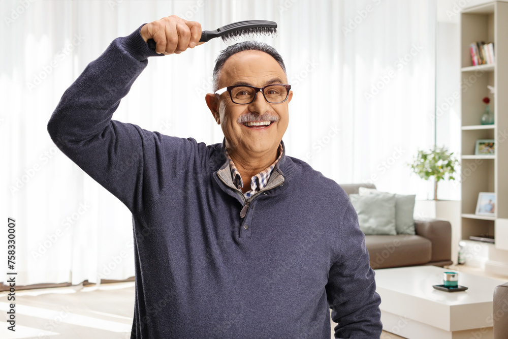 Mature man holding a hair brush bove head at home in a living room Mature man holding a hair brush bove head at home in a living room