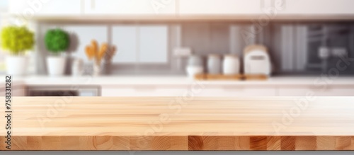 A blurry photo of a kitchen featuring a rectangular wooden table in the foreground. The room has hardwood flooring with a wood stain and varnish finish