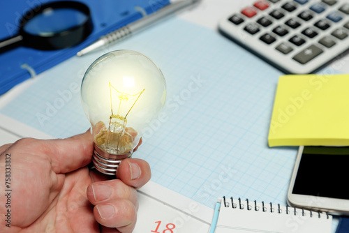 hand holding light bulb in front of desk, business concept
