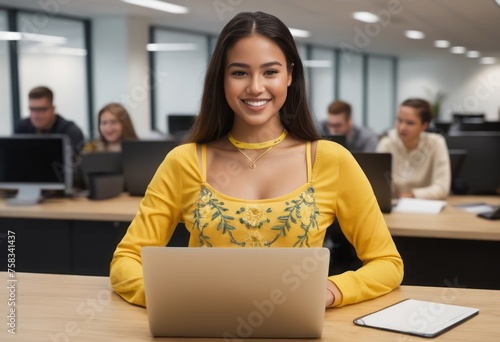 A smiling woman in a yellow top works on a laptop, her joyful demeanor enhancing the office's collaborative spirit.