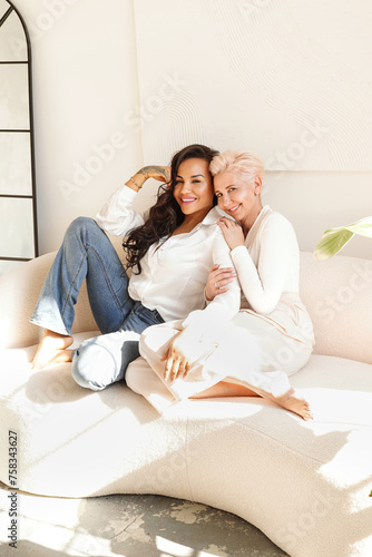 Two women relaxing together in living room, talking and laughing. Female friendship concept