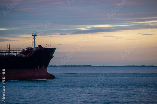 Cargo ship sailing at sunset on Western Scheldt river towards North Sea, seen from boulevard, Vlissingen, Zeeland, The Netherlands.