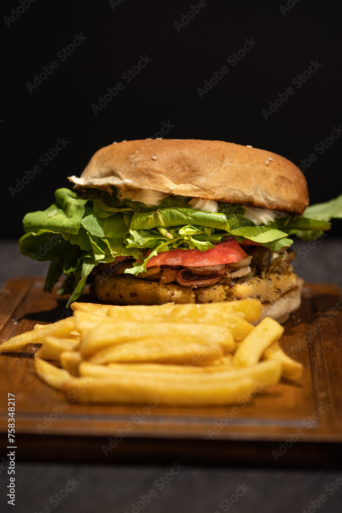 Delicious vegan burger containing chives, mushrooms, tomato, arugula, basil pesto and vegan mayonnaise with French fries