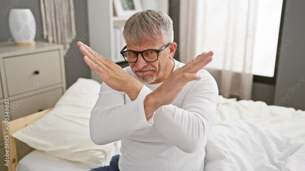 Rejection strikes home, a middle-aged, grey-haired man expresses angry rejection, wearing pyjamas and crossing arms in a bedroom setting Rejection strikes home, a middle-aged, grey-haired man expresses angry rejection, wearing pyjamas and crossing arms in a bedroom setting