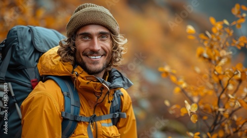 Smiling person with a backpack outdoors surrounded by autumn foliage, wearing a hat and jacket