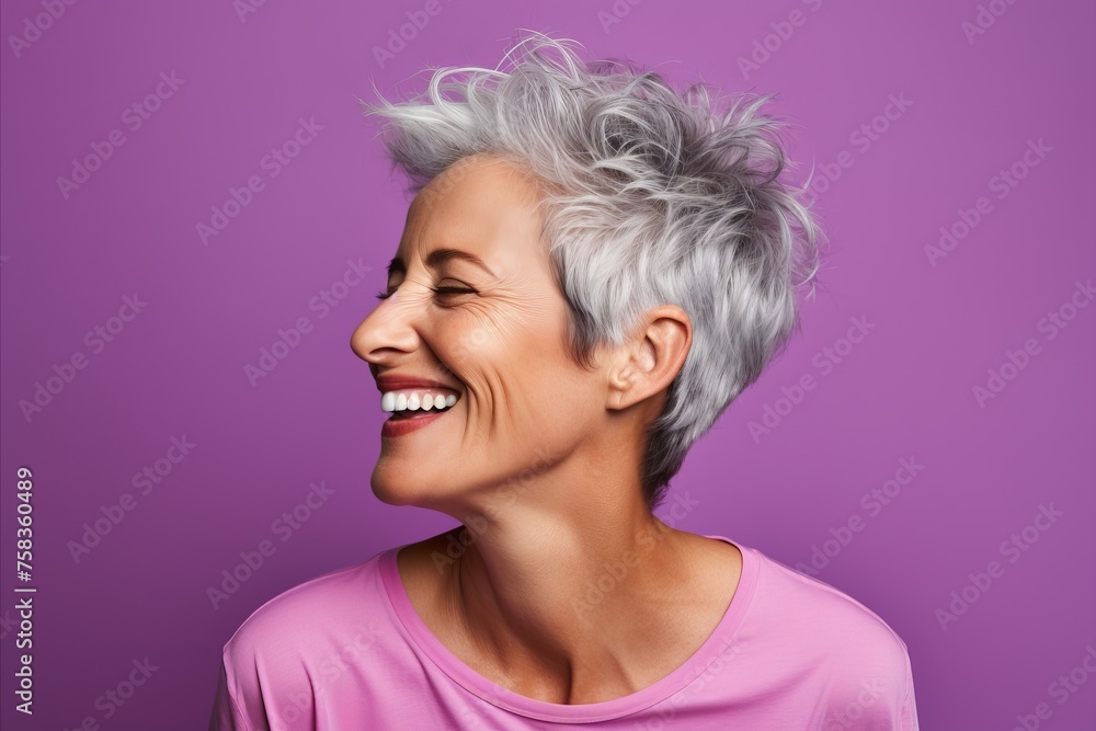 Closeup portrait of a happy senior woman with short grey hair and beautiful smile against violet background