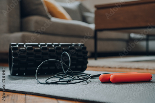 Jump rope and a foam roller on a fitness mat, modern living room, selective focus. photo