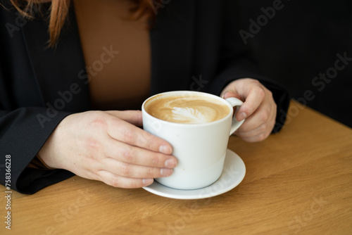Woman s Hands holding a cup of coffee over table. Still life with cup of latte. Coffee in ceramic white cup on wooden table in cafe