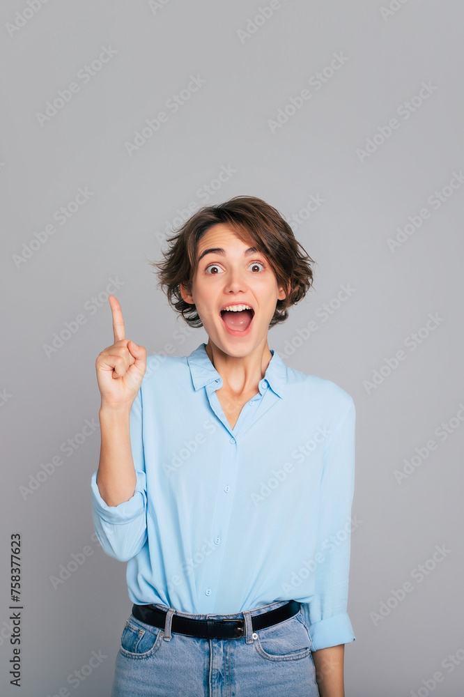 Good offer and idea. Shocked girl pointing above shows place for your advertising text smiles pleasantly wears smart casual isolated over gray background Good offer and idea. Shocked girl pointing above shows place for your advertising text smiles pleasantly wears smart casual isolated over gray background