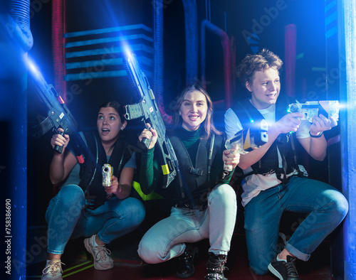 Modern satisfied young people with laser pistols playing laser tag on dark labyrinth