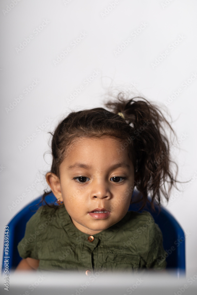 Beautiful 2 years old Latina girl of Mexican mother and Cuban father sitting focused, looking at the laptop Beautiful 2 years old Latina girl of Mexican mother and Cuban father sitting focused, looking at the laptop