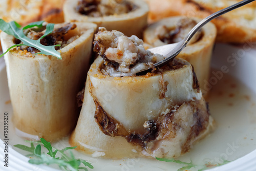Close up Bone Marrow in beef broth with spoon on plate grey background. Side View.
