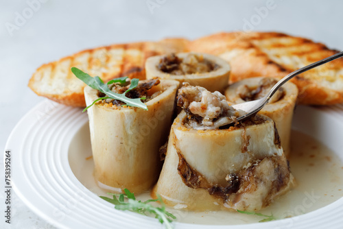 Grill Bone Marrow in beef broth with croutons and spoon on white plate grey background. Side View. Close up.