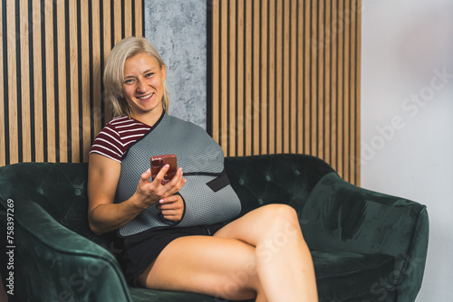 smiling Caucasian woman with a sling on her broken hand sitting on the sofa and holding a phone. High quality photo photo